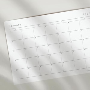 May include: A white paper wall calendar for January 2027 with a minimalist grid layout. The calendar features black text for the month, year, and dates, organized into rows and columns for each day of the week, with thin black lines separating the boxes.