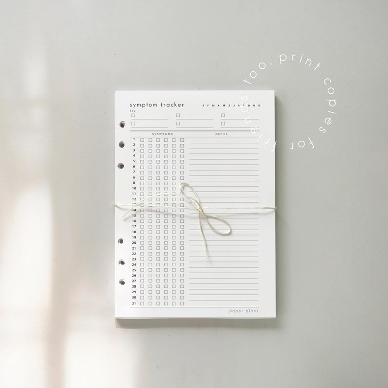 May include: A white symptom tracker notepad with a minimalist design. The notepad features a grid for tracking symptoms and notes, with the text "symptom tracker" at the top. The pages are bound with a string. The words "too. print copies for" are in a circle.