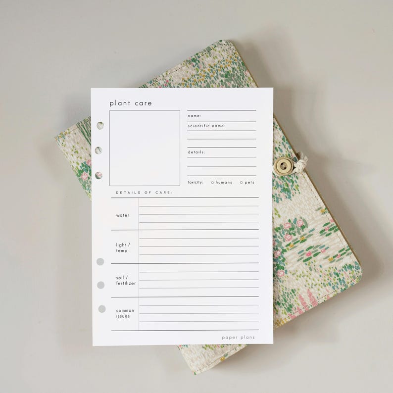 May include: A white plant care planner with a floral patterned cover. The planner includes sections for name, scientific name, details, and care instructions. The cover is a light green and pink floral pattern with a button closure. The text "plant care" and "paper plans" are visible.