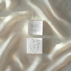 May include: Two small, white square boxes. The top box is open, revealing text that reads "send a voice message today to someone you wouldn't normally" with a sound wave graphic. The bottom box has a heart illustration and the word "VULNERABILITY".