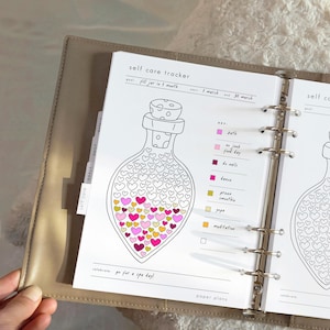 May include: A planner page with a self-care tracker. The tracker features a bottle illustration filled with heart shapes in pink, yellow, and orange. The text includes "self care tracker", "fill jar in 1 month", and "go for a spa day!"