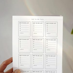 Może przedstawiać: Biała kartka papieru z siatką dziewięciu prostokątnych pól, z których każde oznaczone jest czarnym napisem NOT TO DO LIST. Każde pole zawiera cztery pola wyboru z poziomymi liniami oraz dolną sekcję z napisem celebrate.
