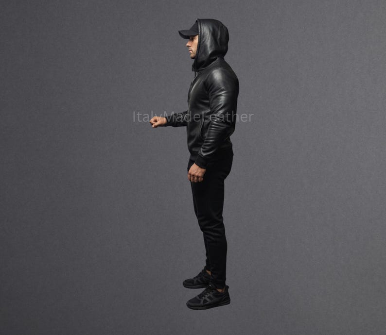 May include: A black leather hooded jacket with matching black pants and a black baseball cap. The jacket has a zipper closure and the hood is up. The person is wearing black sneakers.
