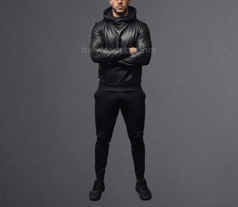 May include: A person wearing a black leather hoodie with a high collar and matching black pants. The hoodie has a sleek, modern design. The outfit is all black, creating a monochromatic look. The person is standing in front of a gray background.