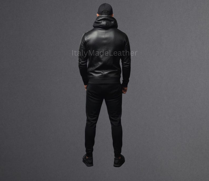 May include: A black leather hoodie and matching black pants. The hoodie has a hood and a zipper closure. The pants are fitted. The person is wearing a black baseball cap. The text "Italy Made Leather" is visible.