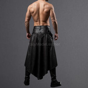 May include: Black leather skirt with a unique asymmetrical design. The skirt features decorative metal studs and a flared, flowing silhouette. The garment is paired with black leather pants and boots. The image is set against a gray backdrop.