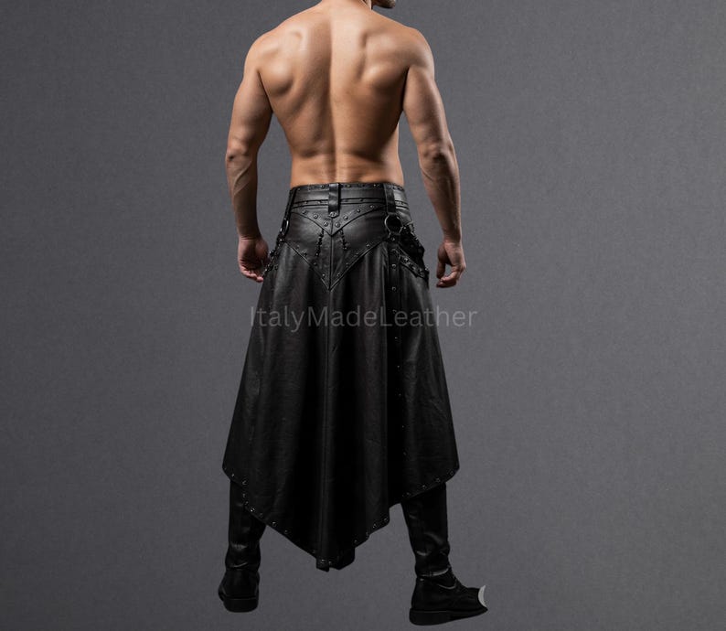 May include: Black leather skirt with a unique asymmetrical design. The skirt features decorative metal studs and a flared, flowing silhouette. The garment is paired with black leather pants and boots. The image is set against a gray backdrop.