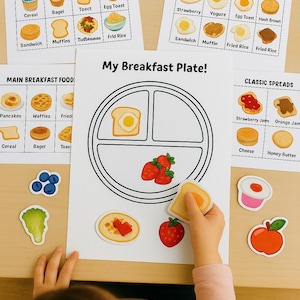 Może przedstawiać: Zestaw edukacyjnych arkuszy ćwiczeń zatytułowanych Main Breakfast Foods, Fruits & Drinks oraz My Breakfast Plate, zawierających ilustracje różnych produktów spożywczych z etykietami. Zawiera luźne wycięte elementy jedzenia, takie jak jagody, sałata i tost.