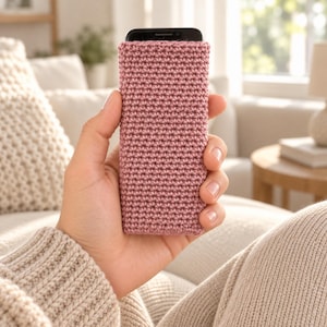 Può includere: Una custodia rettangolare per telefono cellulare con un esterno lavorato all'uncinetto in rosa antico e un motivo a maglia denso e uniforme. La custodia è progettata per adattarsi perfettamente allo smartphone, coprendo il retro e i lati.