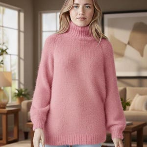 May include: A pink turtleneck jumper with long sleeves. The jumper has a soft, fuzzy texture and a ribbed collar and cuffs. The model is wearing light blue jeans.