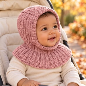 May include: A dusty rose knitted balaclava hood with a ribbed texture that covers the head and neck. The garment features a snug fit around the face and a wide, circular ribbed collar that rests over the shoulders, providing full coverage.