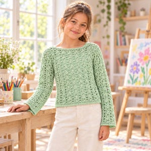 May include: A light green long-sleeve sweater featuring an intricate openwork crochet pattern with a boat neckline and straight hem, paired with plain off-white trousers. The garment has a textured, airy construction with fitted sleeves.