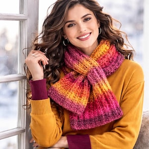 May include: A colorful knitted scarf in shades of pink, orange, and yellow. The scarf is wrapped around the neck and is paired with a mustard yellow sweater with burgundy cuffs. The scarf appears to be hand-knitted.