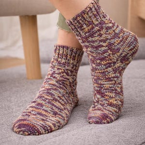 May include: A pair of knitted socks in shades of purple, yellow, and gray. The socks have a ribbed cuff and a textured, striped pattern. The socks are thick and appear to be warm.