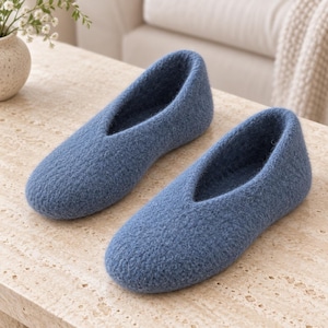May include: A pair of blue felted wool slippers with a rounded toe and a deep V-shaped opening at the instep. The slippers feature a textured, fuzzy surface and a solid blue color throughout, with a simple slip-on design and no visible closures.
