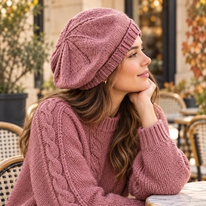 May include: A dusty rose knitted beret with a ribbed brim and a central star-like pattern on the crown, paired with a matching long-sleeved sweater featuring a vertical cable knit design on the sleeves and a simple crew neckline.