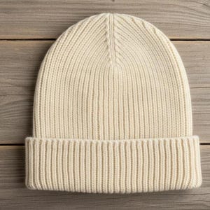 May include: Cream-colored ribbed knit beanie hat. The hat features a folded brim and a close-fitting design. The hat is made of a soft, warm material, perfect for cold weather. The hat is a versatile accessory for any wardrobe.