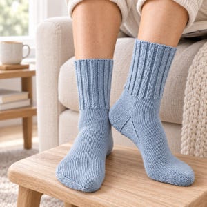 May include: A pair of light blue knit socks featuring a ribbed cuff design that extends down the ankle. The socks are constructed with a visible knit texture, showcasing a reinforced heel section and a smooth toe area in a consistent solid colour.
