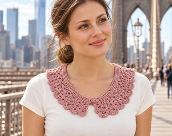 May include: A dusty rose crochet collar featuring a scalloped edge and a small matching button closure at the center front, worn over a plain white short-sleeved t-shirt. The accessory has a detailed, intricate openwork pattern throughout.
