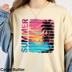 May include: Butter-colored t-shirt featuring a vibrant summer scene. The design includes a sunset over the ocean, palm trees, and the word "SUMMER" in vertical, colorful letters. A seagull flies over the water.