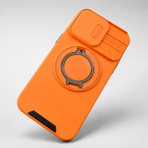 Pode incluir: Uma capa de telemóvel cor de laranja brilhante com uma tampa deslizante para a lente da câmara com o texto em relevo DISCOVER INNOVATION. A capa inclui um anel de suporte metálico circular integrado e um pequeno detalhe preto na base.