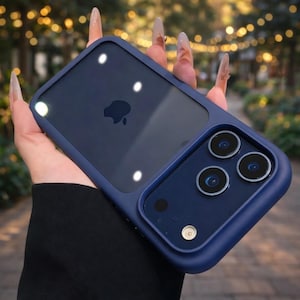 Puede incluir: Una funda de teléfono azul marino con la parte trasera transparente y un marco azul marino. La funda tiene un recorte para la cámara con tres lentes y un flash. El logotipo de Apple es visible en la parte posterior del teléfono. La funda está diseñada para proteger el teléfono.