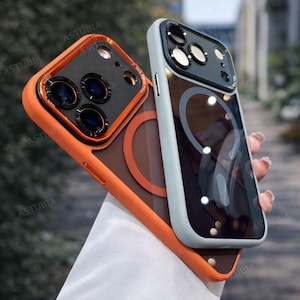 Könnte beinhalten: Zwei Handyhüllen. Eine ist orange mit einem schwarzen Kameraschutz. Die andere ist hellgrau mit einem schwarzen Kameraschutz. Beide Hüllen haben eine transparente Rückseite mit einem kreisförmigen Design.