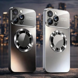 May include: Two metallic phone cases, one bronze and one silver, with a circular design and a camera array. The cases have the word "AUTOFOCUS" printed on them. The background is blurred, suggesting an urban setting.