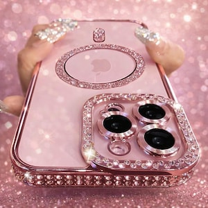 Puede incluir: Funda de teléfono rosa con marco dorado rosa y brillantes pedrería. La funda tiene una parte trasera transparente con un recorte del logotipo de Apple y un anillo decorativo alrededor de las lentes de la cámara. La funda está diseñada para proteger el teléfono.
