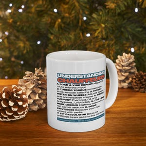 Puede incluir: Taza de cerámica blanca con el texto "UNDERSTANDING CHAUFFEURS" en azul, rojo y naranja. La taza enumera 7 cualidades de un chófer, incluyendo "Road & Vibe Expert" y "Silent Support". La taza está sobre una superficie de madera con piñas en el fondo.