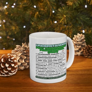 Könnte beinhalten: Weiße Keramiktasse mit dem Text "UNDERSTANDING PEST MANAGEMENT PROFESSIONAL (PMP)" in Grün und Schwarz. Die Tasse hat eine Liste von Schädlingsbekämpfungsbegriffen. Die Tasse steht auf einer Holzoberfläche mit Tannenzapfen.