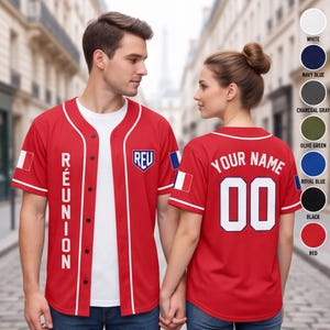 May include: A red baseball jersey with white piping, featuring the text REUNION vertically on the front, a shield logo with REV, and a French flag on the sleeve. The back displays the text YOUR NAME and the number 00 in white with blue outlines.