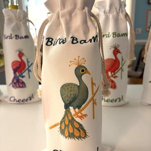 May include: White fabric wine bottle bags with drawstring closures. Each bag features a colorful illustration of a bird and the text "Bird Bam" and "Cheers!". The bird illustrations are in shades of red, green, and yellow.