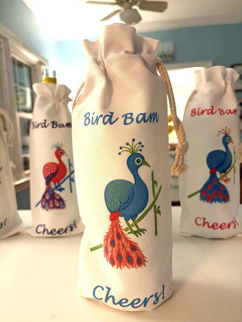 May include: White fabric wine bottle bags with a drawstring closure. Each bag features a colorful peacock illustration with the text "Bird Bam" and "Cheers!". The peacock has blue, red, and green accents.