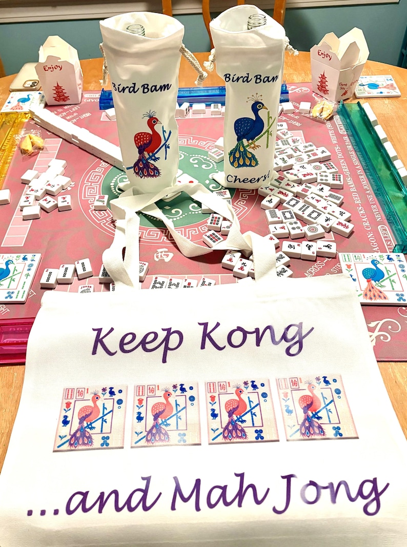 May include: A Mahjong game setup with tiles, two white bottle bags with peacock designs and the text "Bird Bam" and "Bird Ban". A white tote bag with the text "Keep Kong ...and Mah Jong" is in the foreground.