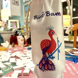 May include: White fabric wine bottle bag with a drawstring closure. The bag features a red and purple bird illustration with the text "Bird Bam" and "Cheers!" in purple script. A fun gift.