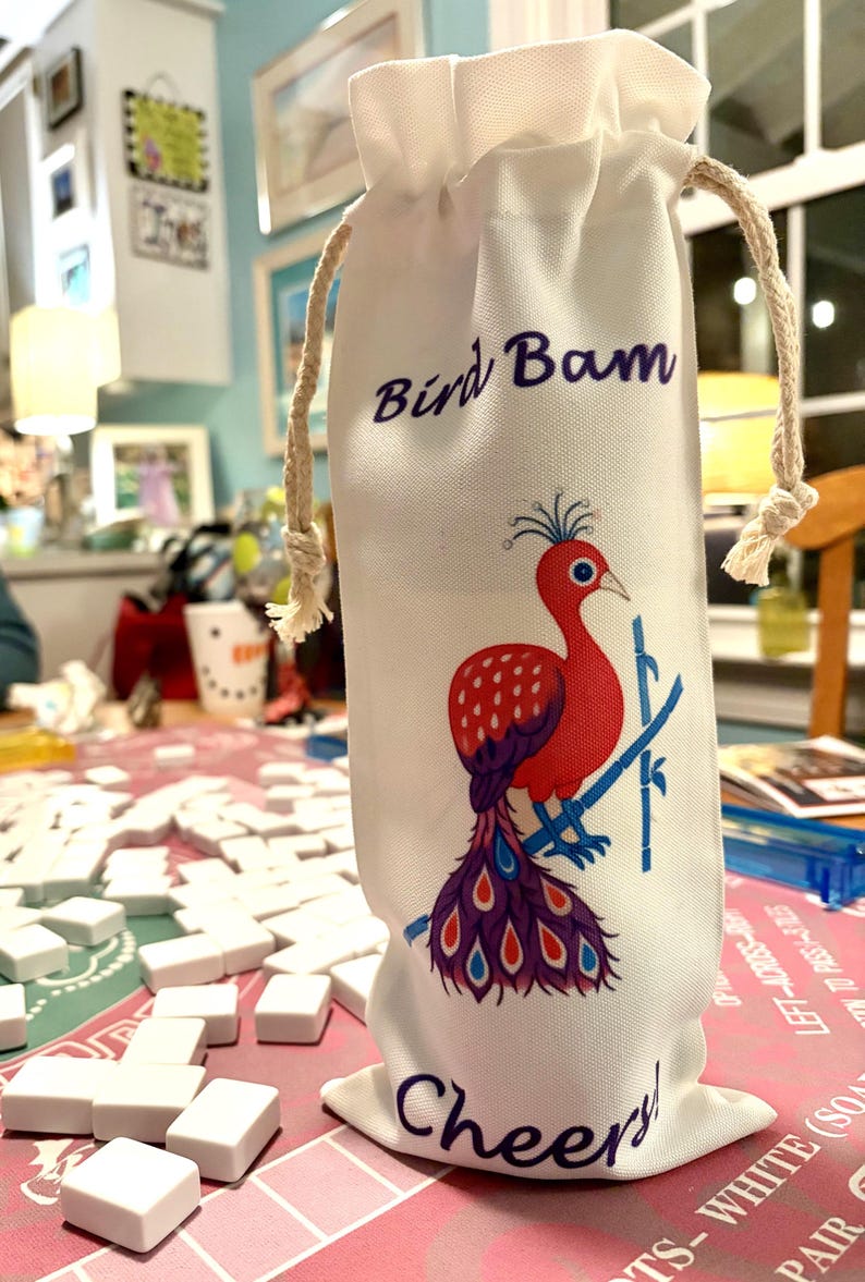 May include: White fabric wine bottle bag with a drawstring closure. The bag features a red and purple bird illustration with the text "Bird Bam" and "Cheers!" in purple script. A fun gift.