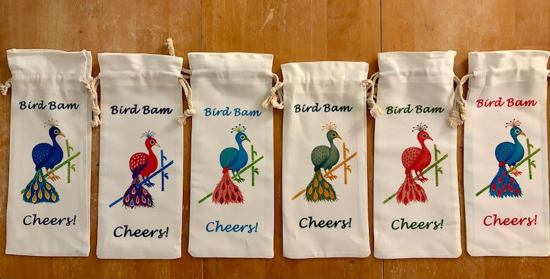 May include: Six white wine bottle bags with drawstring closures. Each bag features a colourful peacock illustration with the text "Bird Bam" and "Cheers!". The peacock designs vary in colour, including blue, red, and green.
