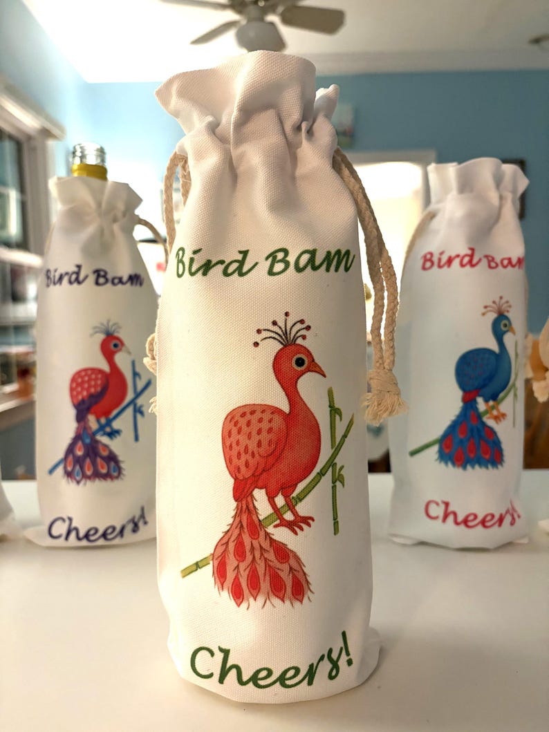 May include: White wine bottle bags with peacock designs in red, blue, and pink. The text "Bird Bam" and "Cheers!" are printed on the bags. The bags have a natural rope drawstring closure.