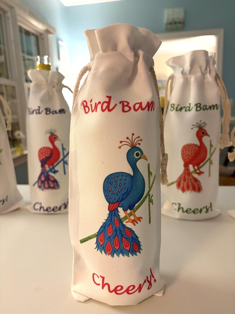 May include: White drawstring wine bottle bags featuring a peacock illustration in blue, red, and green. The text "Bird Bam" and "Cheers!" are printed on the bags. The bags are made of a soft fabric.