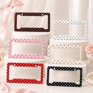 May include: A collection of six rectangular license plate frames featuring various polka dot patterns. The frames are available in brown, white, pink, cream, red, and black, each with contrasting dots and four mounting holes for attachment.