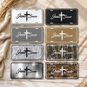 May include: Eight rectangular license plates featuring the text Jesus Saves and a cross graphic. The plates come in various finishes including solid white, black, gray, tan, metallic silver, gray camouflage, green camouflage, and brown camouflage.
