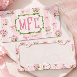 May include: A rectangular license plate and a matching license plate frame featuring a pink and white vertical striped background with pink hydrangea flowers and light pink bows. The plate displays the monogram MFC in pink inside a green bamboo frame.