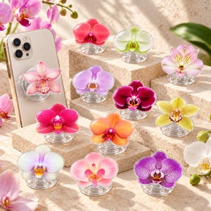 May include: A collection of circular phone grips featuring various orchid flower designs in shades of pink, purple, yellow, orange, and white. One grip is attached to a light-colored smartphone, while others are displayed on stone blocks.