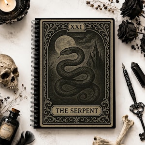 May include: A spiral-bound notebook featuring a dark, illustrated cover with a large snake, a full moon, and a gothic building. The text 'XXI' and 'THE SERPENT' are printed in a gold-toned font within an ornate, decorative border frame.