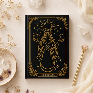 Peut inclure: Un carnet à couverture rigide noire avec des lignes dorées représentant une figure centrale tenant un soleil et une lune, un croissant de lune à la base et un soleil au-dessus. Le texte THE GODDESS est imprimé en or dans une bordure décorative.