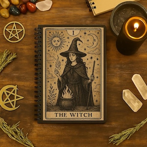 May include: A spiral-bound notebook featuring a tarot card illustration of a witch with a sun and moon design. The notebook is surrounded by crystals, a lit candle, and other mystical items on a wooden surface.