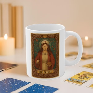 May include: White ceramic mug featuring a tarot card design. The card depicts a nurse in a red coat and white cap, holding a bowl and a tool. The card is framed with floral and scroll details, with the text "THE NURSE".