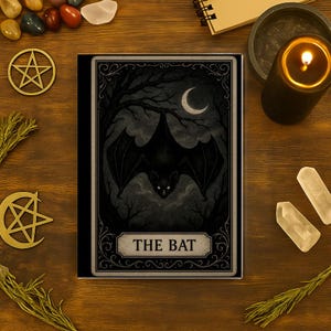 Op de afbeelding: Een tarotkaart met een zwarte vleermuis met gloeiende ogen, tegen een donkere, maanverlichte bosscène. De kaart is gelabeld "THE BAT" in een decoratieve banner. De afbeelding is omgeven door kristallen, een brandende kaars en andere mystieke items.