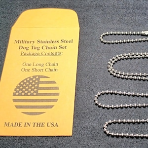 May include: A military stainless steel dog tag chain set. The set includes one long chain and one short chain. The chains are silver and made of small, round beads. The set comes in a yellow envelope with text and an American flag.